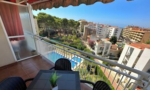Un balcon donnant sur un quartier résidentiel, une piscine et une table avec des chaises.