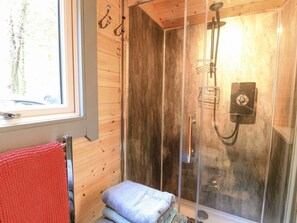 Puinen mökki, jossa on lasiseinällä varustettu suihku, ikkuna ja punainen pyyhe metallisella pyyhetelineellä.