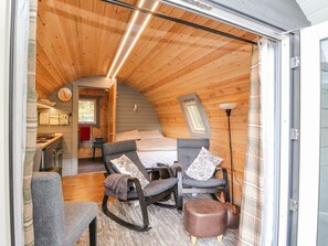 A cozy cabin interior with a bed, two chairs, a small table, and a lamp. - Elleric Pods - The Last Resort (Appin)