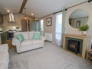 A living room with a white sofa, a fireplace, a kitchen in the background, and a large mirror on the wall. - Owl, Shobdon Herefordshire (Leominster)