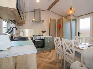 A modern kitchen with a built-in oven, a dining area with white chairs, and a large window providing natural light. - Owl, Shobdon Herefordshire (Leominster)