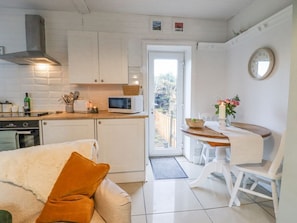 A compact kitchen with white cabinets, a microwave, and a stove. There's a dining area with a table and chairs, and a small window. - Penny Cottage, West Yorkshire. (Keighley)