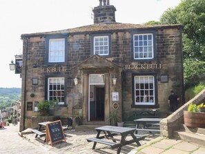 A stone building with 'BLACK BULL' signage, outdoor seating, and a signboard with menu items. - Penny Cottage, West Yorkshire. (Keighley)