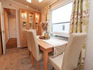 Ein Essbereich mit Holztisch, Stühlen, einer Vase mit Trockenblumen und einem Fenster mit Vorhängen.