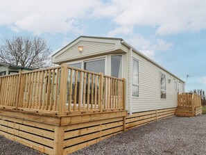 Ein Wohnmobil mit einer Holzterrasse, großen Fenstern und einem Schotterweg.