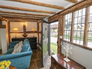 A cozy room with a blue sofa, wooden beams, a wooden dresser, and a window with a view of a stone building. - Church View, Welford-On-Avon (Stratford-upon-Avon)