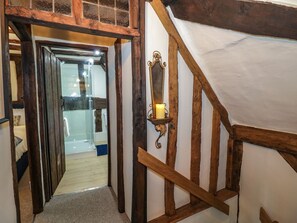 A narrow hallway with wooden beams, a glass door leading to a bathroom, and a wall-mounted candle holder. - Church View, Welford-On-Avon (Stratford-upon-Avon)