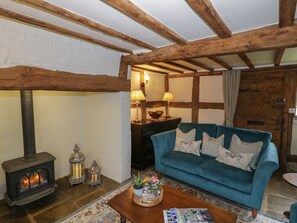 A cozy room with exposed wooden beams, a blue sofa, a wooden coffee table, a fireplace, and a stone wall. - Church View, Welford-On-Avon (Stratford-upon-Avon)