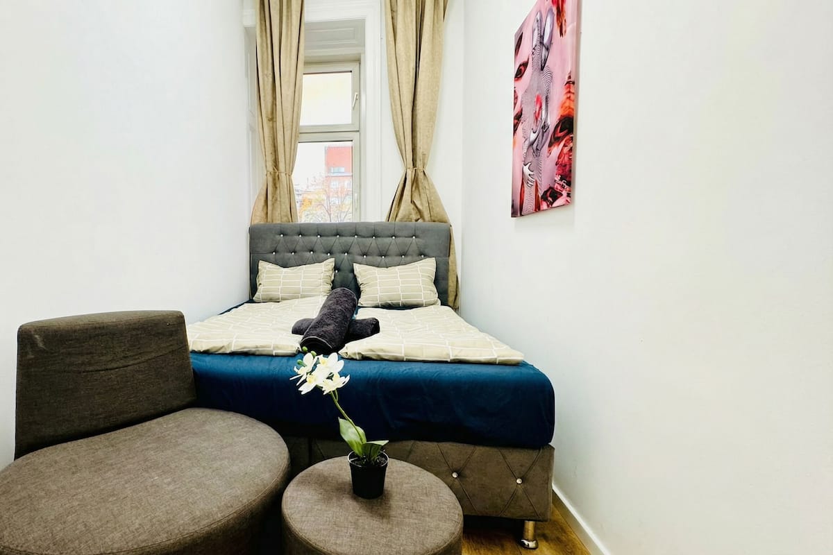 A bedroom with a bed, a chair, a small table, and a potted plant.