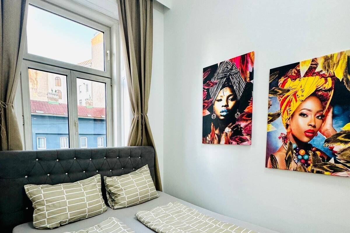 A bedroom with a bed, two pillows, a black blanket, and two paintings on the wall.