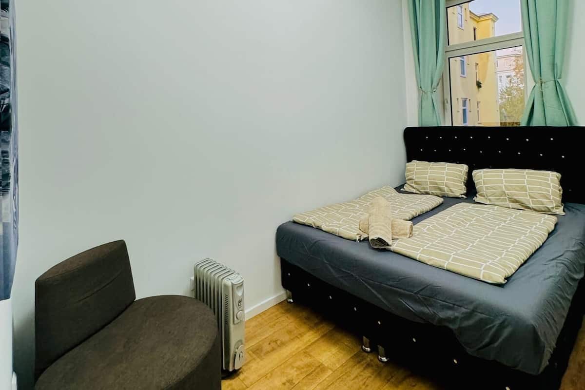 A bedroom with a bed, a chair, a radiator, and a window with curtains.