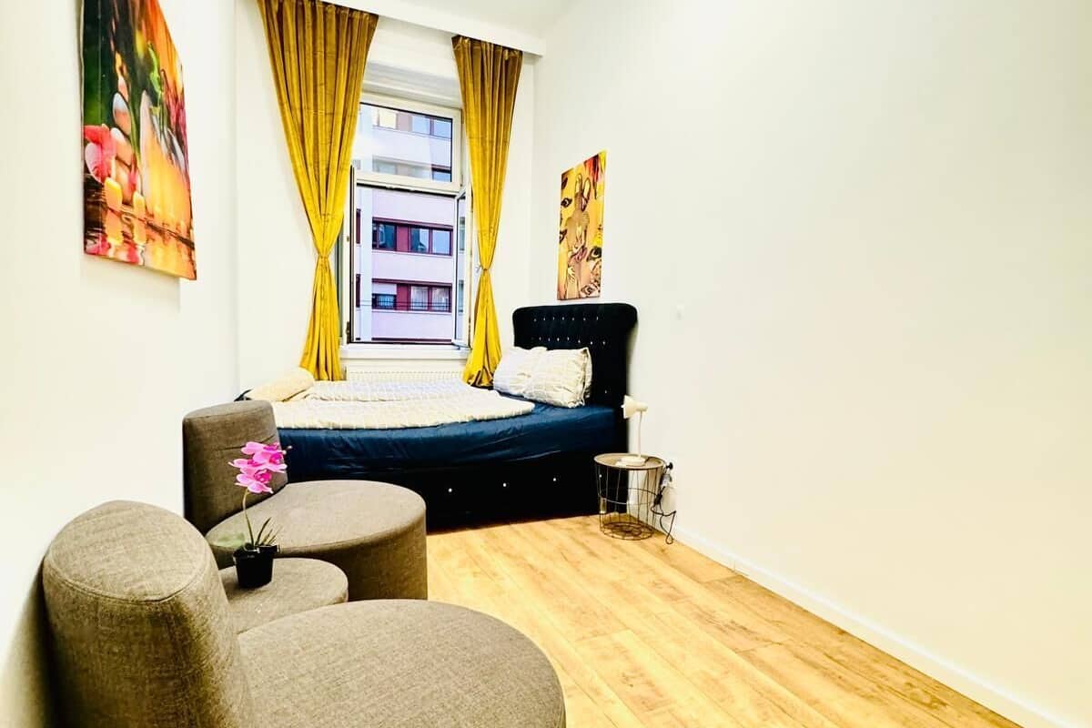A modern bedroom with a bed, a small seating area, and a view of a building outside.