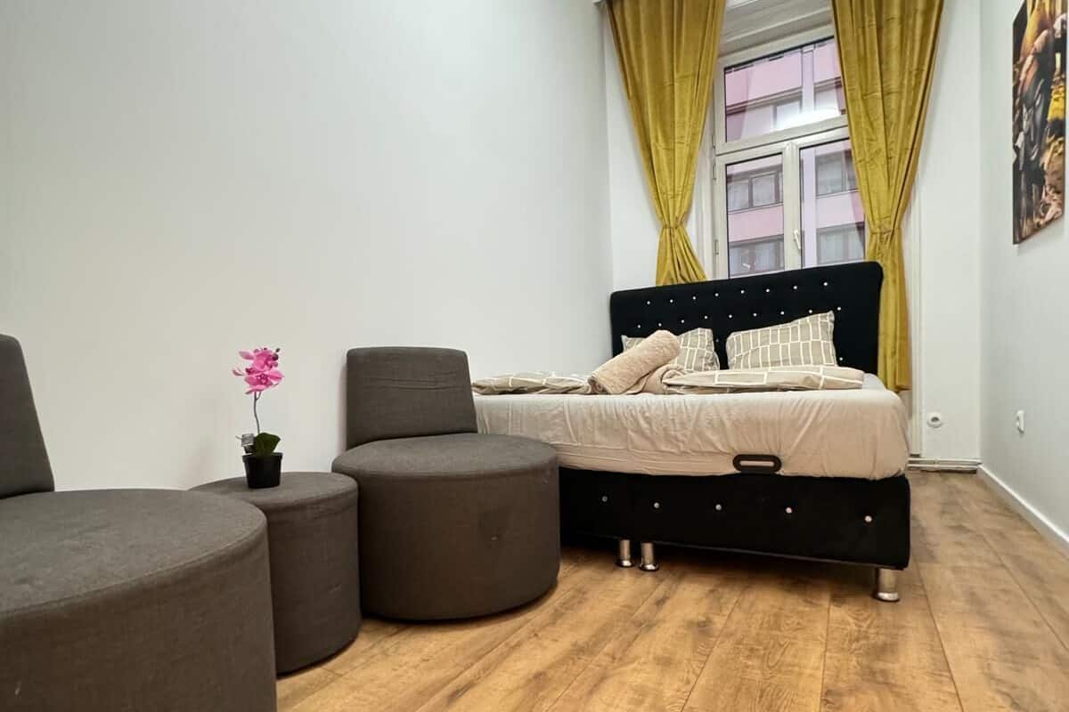 A modern bedroom with a bed, two ottomans, a chair, and a small potted plant.