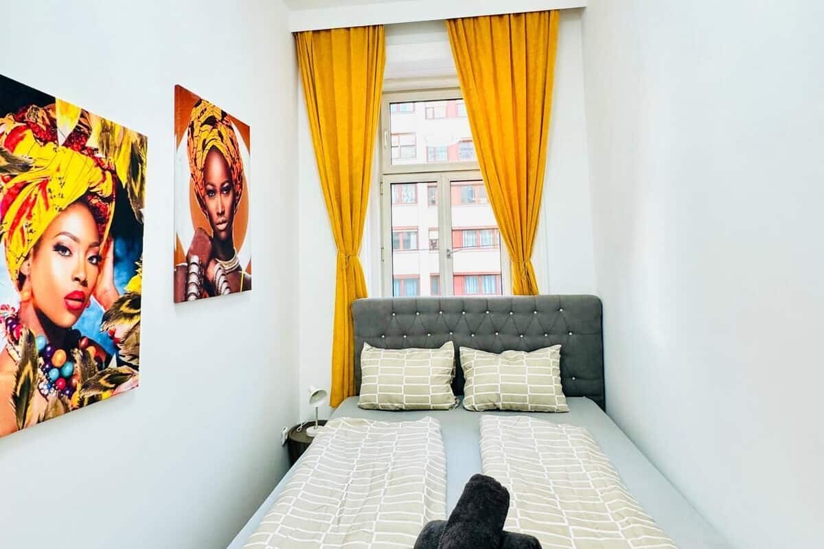 A bedroom with a bed, two pillows, a bedside table, and a window with yellow curtains.