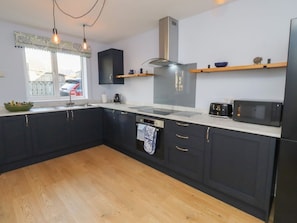 A modern kitchen with dark cabinets, a stainless steel range hood, a microwave, and a window with a view of the outside. - Linn Cottage, Bellingham (Hexham)
