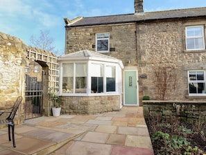 A stone building with a conservatory, a green door, and a bench in the courtyard. - Linn Cottage, Bellingham (Hexham)