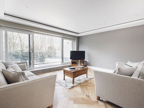 Ein modernes Wohnzimmer mit großem Fenster, einem Flachbildfernseher, zwei Sofas und einem Holztisch.