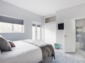 Ein modernes Schlafzimmer mit einem Bett, einem Fernseher, einer Tür zu einem anderen Raum und einem Fenster.