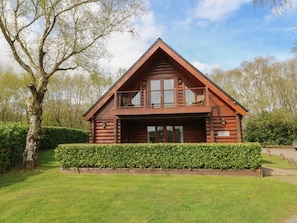 A log cabin with a balcony, surrounded by a well-maintained hedge and a large tree. - Willow in Dolton, Devon. 3 bed (Winkleigh)
