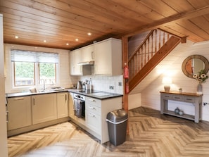 A kitchen with wooden ceiling beams, white cabinets, a herringbone floor, a staircase, and a small console table with decorative items. - Willow in Dolton, Devon. 3 bed (Winkleigh)