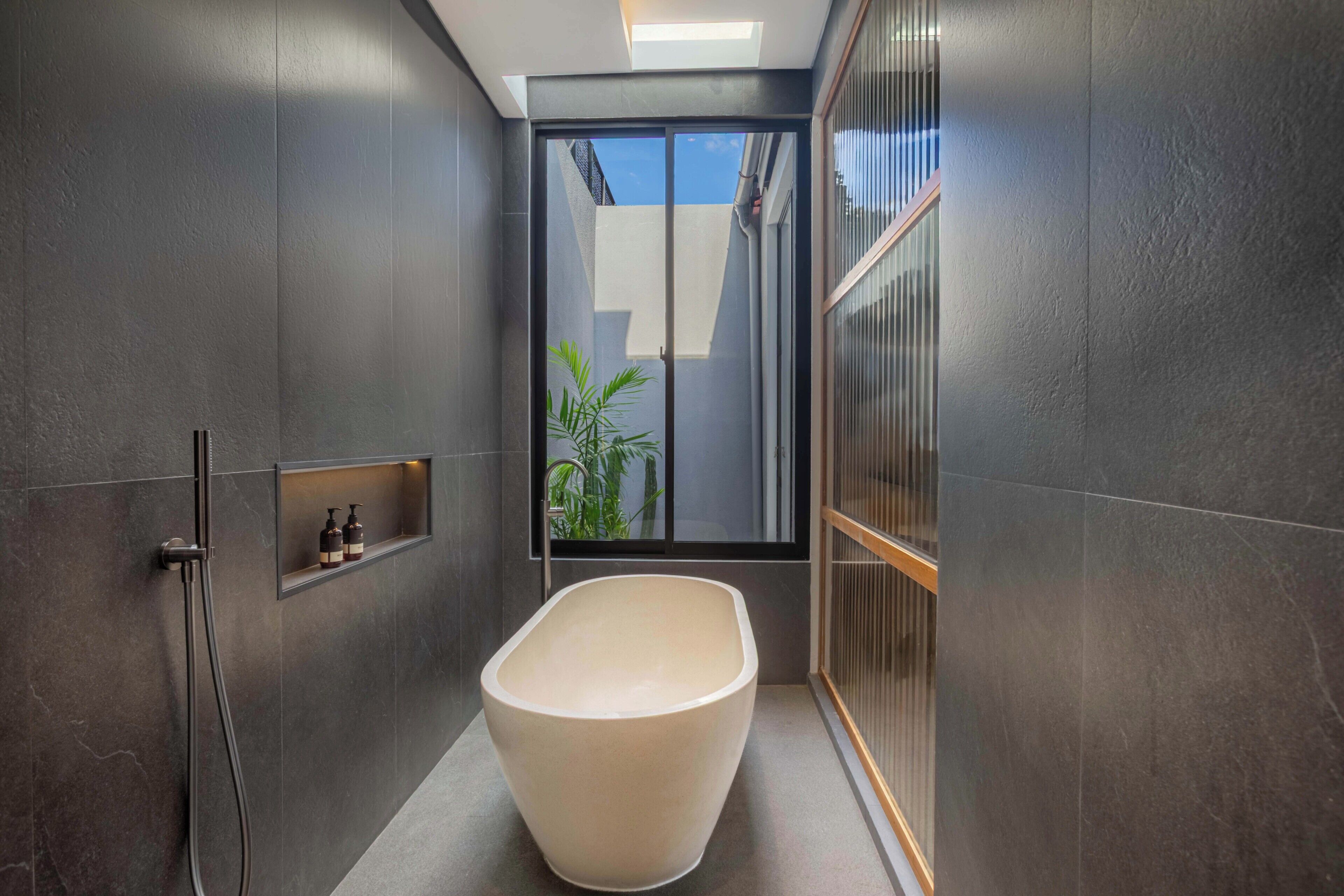 A modern bathroom with a freestanding bathtub, a shower, and a small shelf with toiletries.