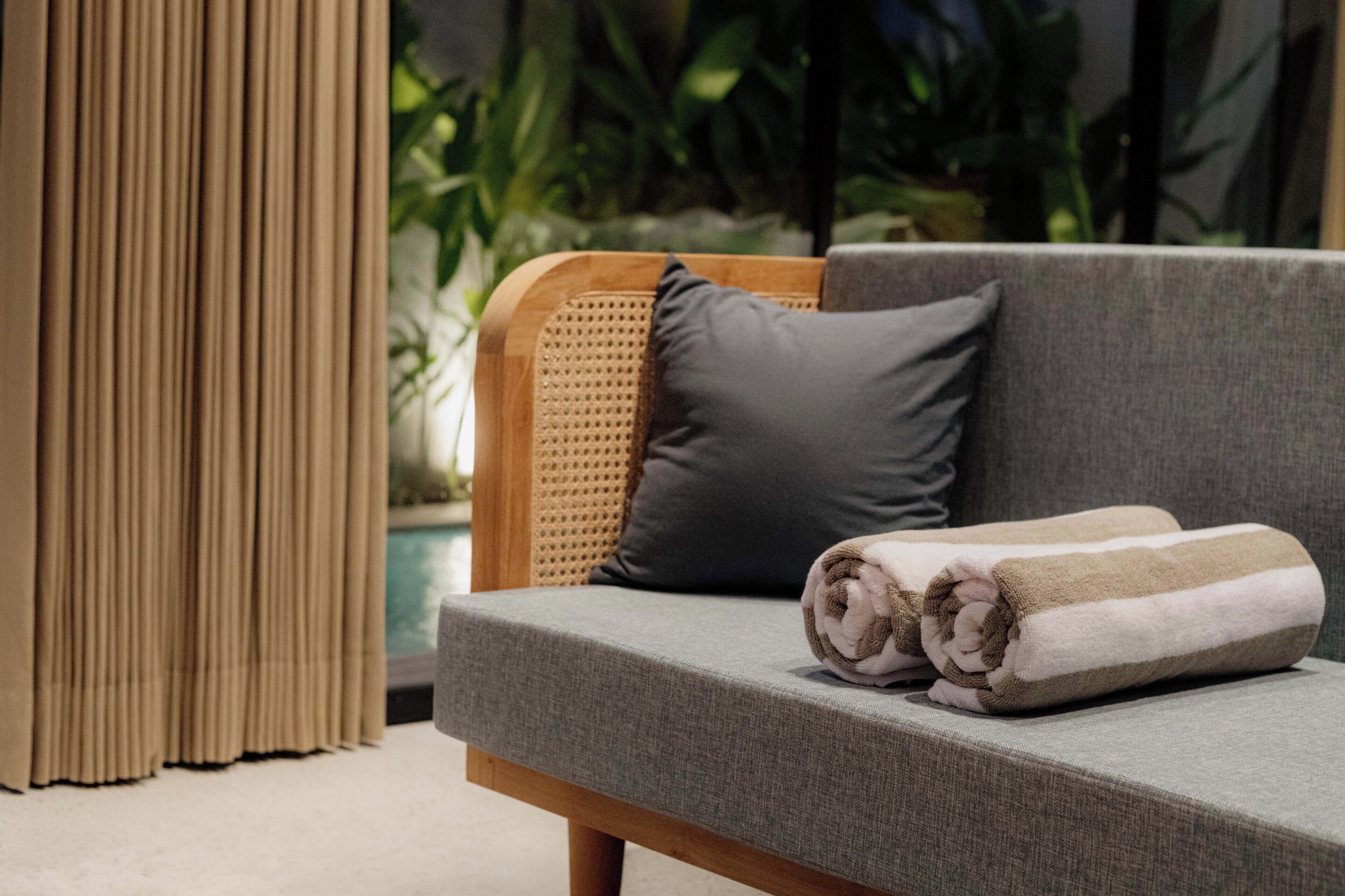A sofa with a rolled towel, a grey cushion, and a woven headrest.
