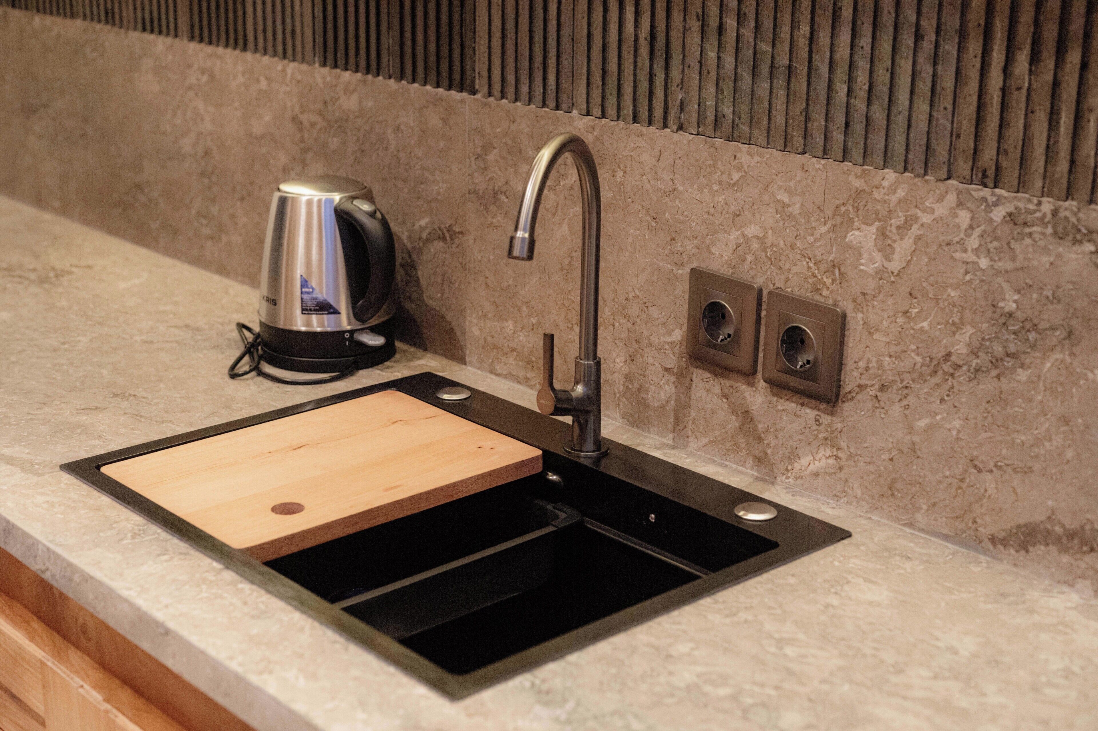 A modern kitchen with a stainless steel sink, a wooden cutting board, and a kettle.