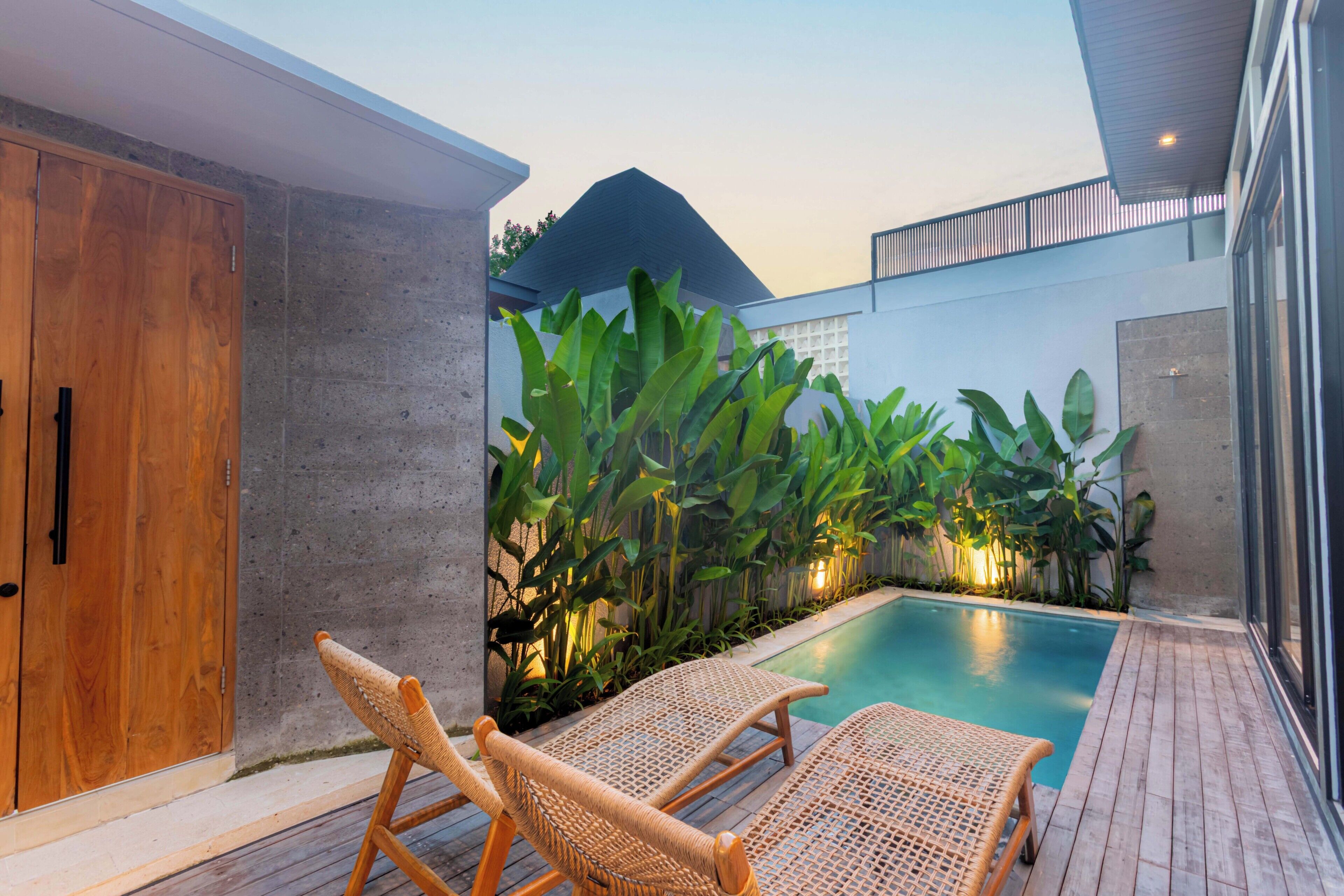 A poolside area with wicker lounge chairs, a concrete wall, and tropical plants.