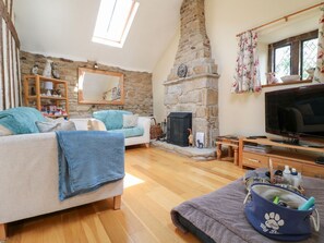 A cozy living room with a stone fireplace, a sofa, a television, and a pet carrier. - 33 Main Road Higham Derbyshire (Alfreton)