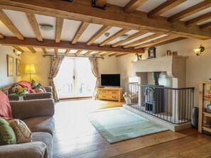 A living room with a sofa, TV, fireplace, wooden beams, and a balcony.