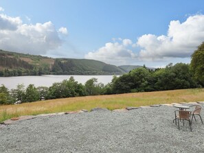 Un área de grava con una mesa y sillas, con vista a un lago y colinas.