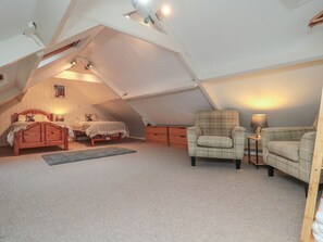A cozy attic bedroom with a sloped ceiling, a wooden bed, two armchairs, a small table, and a lamp. - Providence Cottage Ugglebarnby (Whitby)