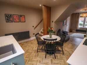 Een moderne keuken met een visgraatvloer, een ronde eettafel met stoelen, een radiator en een trap.