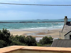 A coastal view with a beach, rocky outcrops, and a lighthouse in the distance. - Swyn Llyr, Rhosneigr, Anglesey (Rhosneigr)