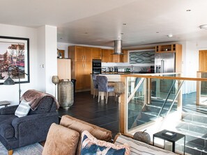 A modern kitchen with wooden cabinets, stainless steel appliances, and a dining area with a blue chair. - Swyn Llyr, Rhosneigr, Anglesey (Rhosneigr)