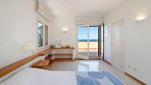 Une chambre d’hôtel équipée d’un lit, d’un bureau, d’une chaise, d’une lampe, d’une fenêtre et d’une porte donnant sur un balcon avec vue sur la plage.