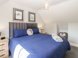A bedroom with a large bed, a nightstand, a lamp, and two framed pictures on the wall.