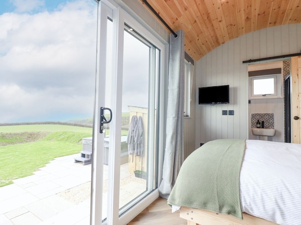 Ein Schlafzimmer mit Bett, Fernseher, Fenster und Blick ins Freie.