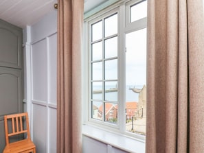 A room with a large window, a wooden chair, and a view of buildings and water. - Steps Cottage, North Yorkshire (Whitby)