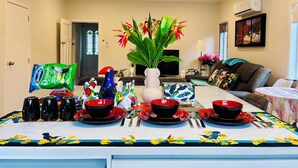 A dining area with a table set for four, a potted plant, and a television in the background. - Sunny 3BR Home - Close to Essentials & Transport (Auckland)