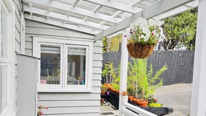 A covered porch with a wooden deck, a white railing, and potted plants. - Sunny 3BR Home - Close to Essentials & Transport (Auckland)