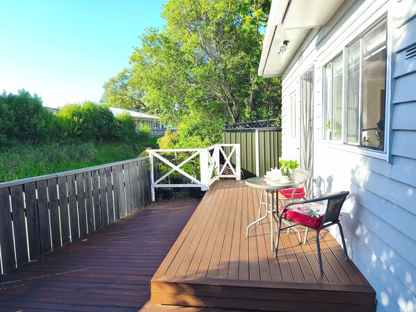 A wooden deck with a white gate, a table with chairs, and a potted plant.