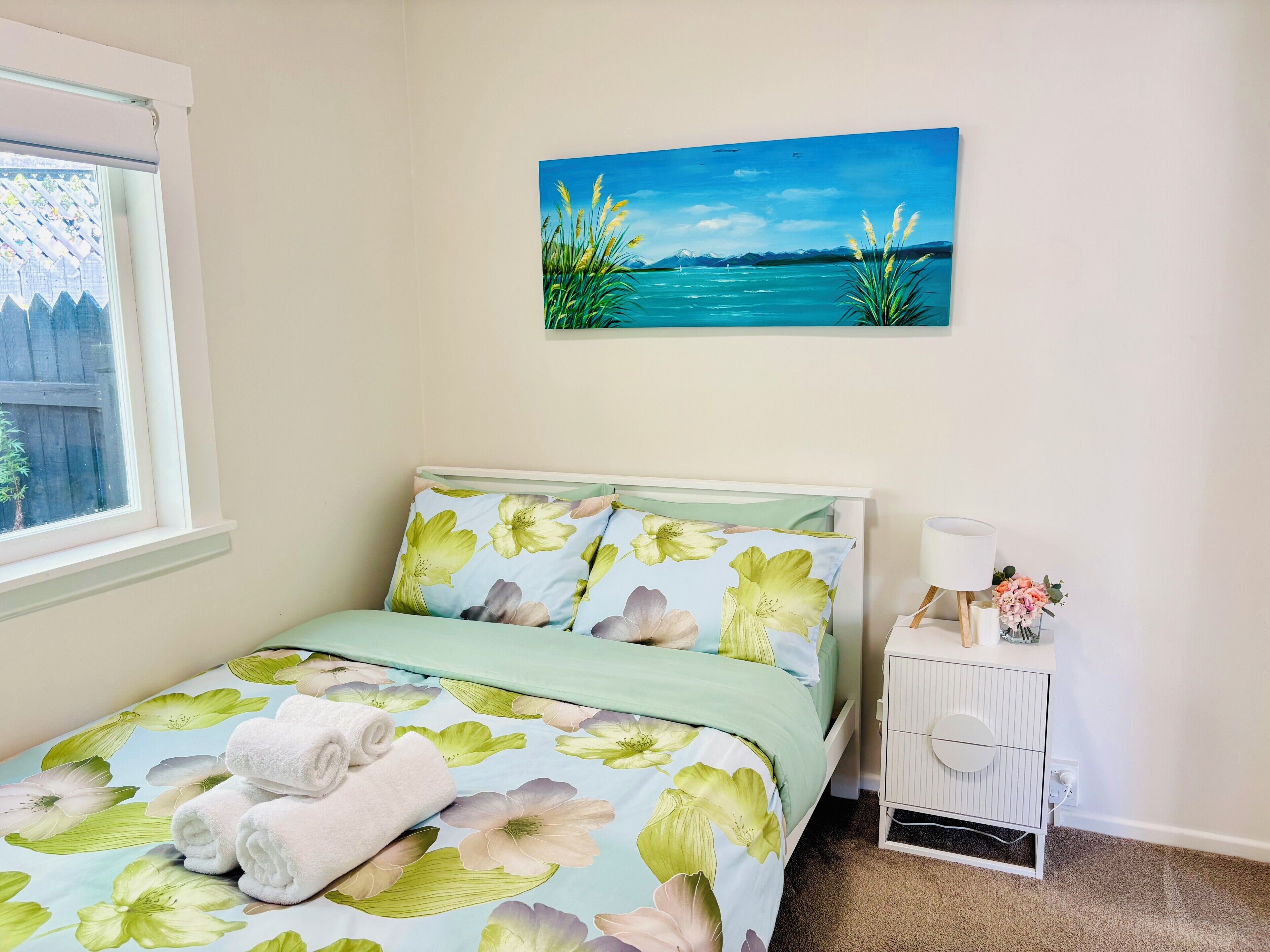 A bedroom with a bed, a nightstand, a lamp, and a painting of a landscape.
