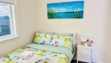 A bedroom with a bed, a nightstand, a lamp, and a painting of a landscape.