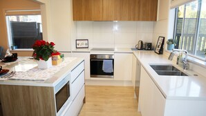 A modern kitchen with white cabinetry, a central island, a built-in oven, and a window with a view. - Sunny 3BR Home - Close to Essentials & Transport (Auckland)