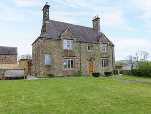 Une maison en pierre avec un toit à deux versants, une porte d’entrée et un petit jardin devant.