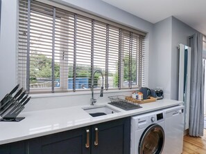Eine moderne Küche mit Waschmaschine, Spüle und einem Fenster mit Jalousien.