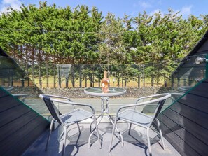 Eine Terrassengaststätte mit zwei Korbstühlen und einem runden Tisch, umgeben von einem Glaszaun, mit Blick auf ein bewaldetes Gebiet.