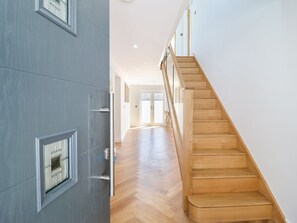 Ein Flur mit einer Holztreppe, einer Tür mit Fenster und einem hellen Boden.