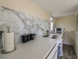 Una cocina con salpicadero de mármol, un lavabo de acero inoxidable, un microondas y una estufa.